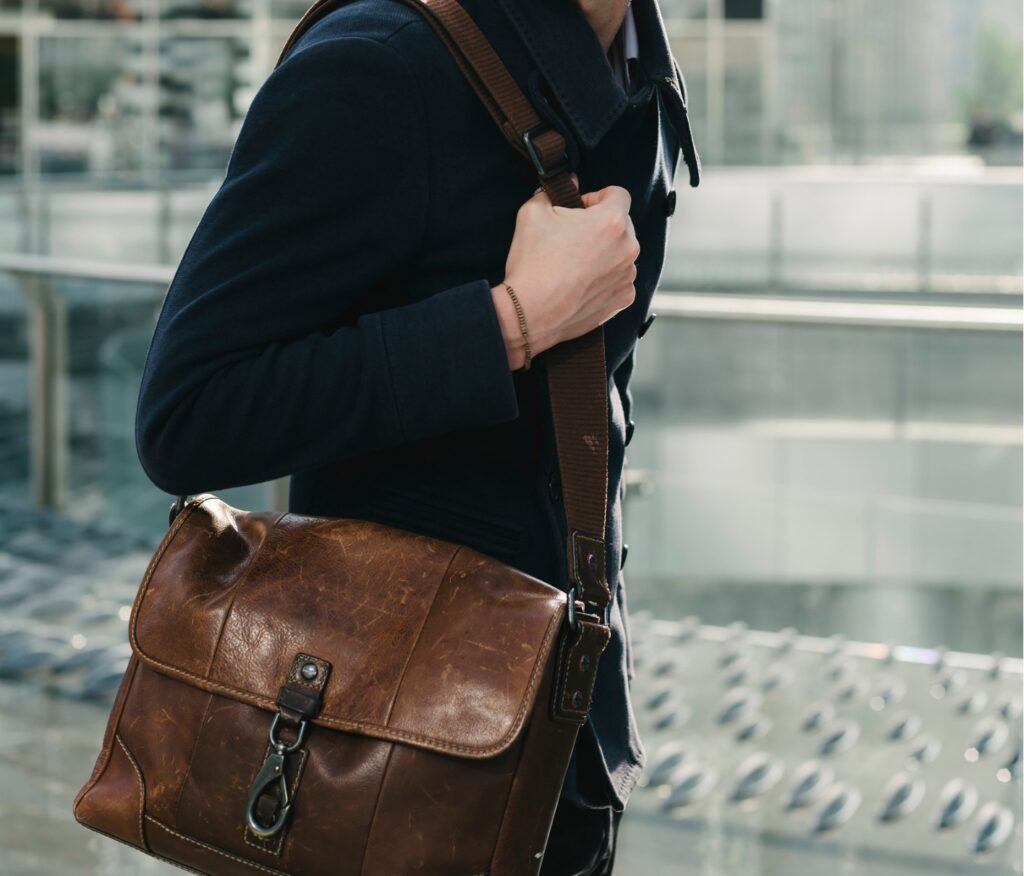 Person carrying a brown leather messenger bag over their shoulder while walking in an urban environment